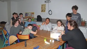 Un groupe d'enfants et leur animatrice observent un récipient éclairé par une lampe torche