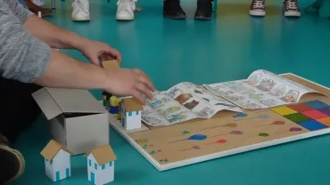 Une personne assise par terre présente un jeu de plateau fait main