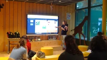 Une animatrice présente un outil pédagogique projeté sur un écran, des adultes sont assis devant 