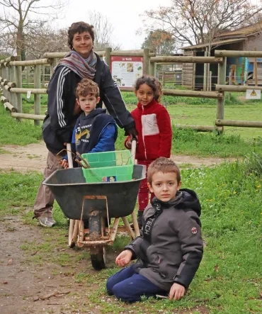 Un groupe d'enfants et leur animatrice sont à l'extérieur avec une brouette