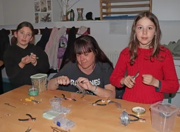 Deux enfants et leur animatrice fabrique des boucles d'oreilles avec des plumes