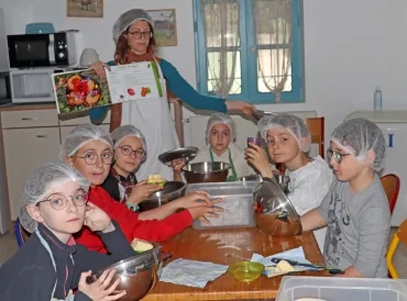 Un groupe d'enfants et leur animatrice sont en cuisine avec charlotte et tablier en train de cuisiner