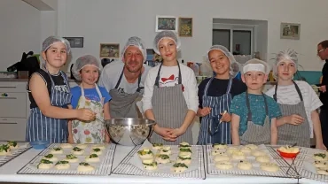 Un groupe d'enfants et leur animateur sont en cuisine avec des tabliers et des charlottes et montrent des petites boules de pâte.