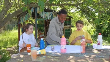 Un groupe d'enfants et leur animateur peignent en exterieur.