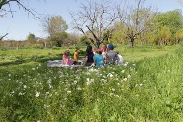 Des enfants et leur animatrice assis sur une couverture dans un pré