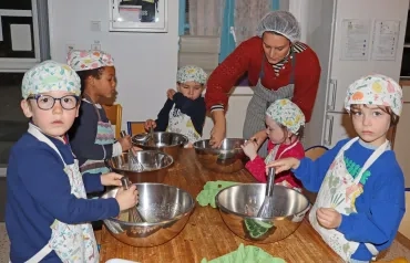 des enfants et leur animatrice, en charlottes et tabliers, mélangent avec leur fouet une préparation