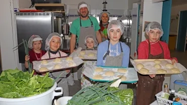 un groupe d'enfants et leur animateur en cuisine avec charlottes et tabliers montrent des légumes verts et des boules de pâte