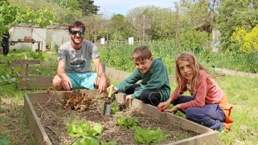 Deux enfants et leur animateur sont devant des salades au potager