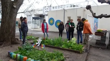 Un adulte présente le jardin pédagogique d'une école à un groupe d'adultes 