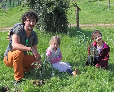deux enfants et leur animateur sont assis par terre avec des poireaux