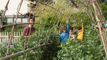 Quatre enfants montrent leurs récoltes de fèves avec leur animateur dans le potager