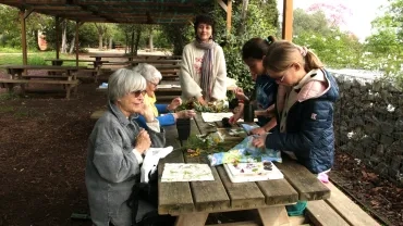Activité intergénérationnelle, l’animatrice, deux enfants et trois personnes âgées crées des Tataki-zomé, empreinte végétale sur du tissu, elles tapent avec un maillet sur le tissu pour crée l’empreinte de la plante leur animatrice