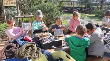 un groupe d'enfant et leur animatrice tissent des morceaux de tissus sur des carrés de bois