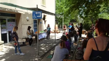 Trois adultes parlent en face d'un groupe d'adultes en extérieur 