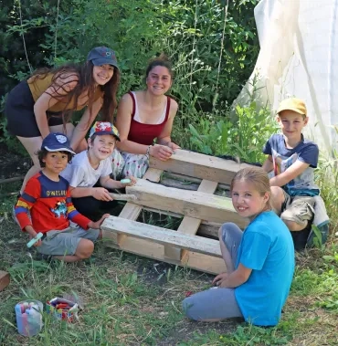 un groupe d'enfants et leurs animatrices utilisent des craies pour colorier du bois de palette