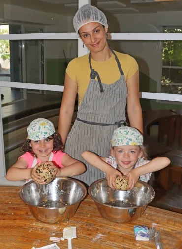 2 enfants et leur animatrice sont en cuisine avec leur chalotte et leur tablier et montrent une boule de pâte.