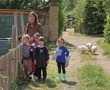 un groupe d'enfants et leur animatrice sortent du potager avec 3 oies derrière eux