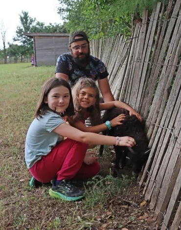 Deux fillettes et leur animateurs sont accroupies près d'un jeune mouton