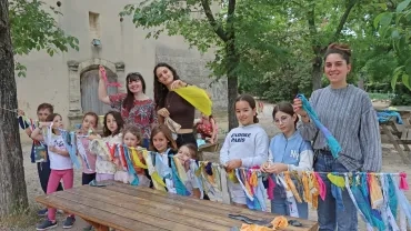 Un groupe d'enfants et leurs animatrices posent devant leur guirlande de morceaux de tissus