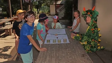 Un groupe d'enfants et leur animatrice déguisée en dinosaure sont devant de grandes feuilles blanches