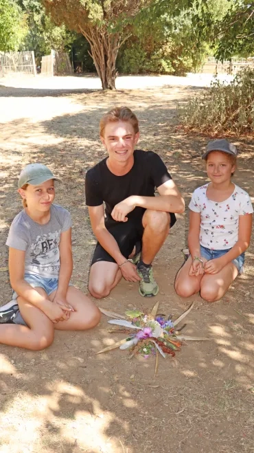Deux fillettes et leur animateur posent avec une réalisation en élément naturel posée au sol