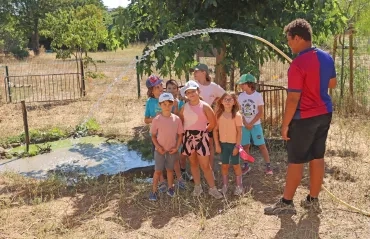 Un groupe d'enfants et leur animateur sont devant la mare des cochons avec un tuyai d'arrosage