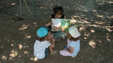 Trois enfants et leur animatrice assis par terre à lire une histoire pendant la balade contée
