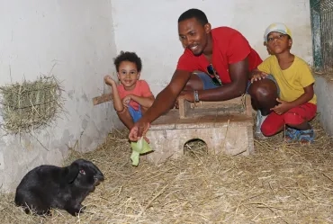 Deux enfants, leur animateur et un lapin sont dans un enclos