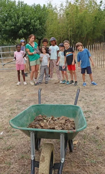 Un groupe d'enfant et une animatrice posent devant une brouette