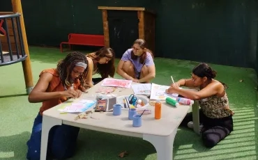 Plusieurs personne sont assis par terre autour d'une petite table et font de la peinture 