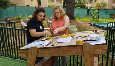 deux personnes sont devant une table où elle réalise un petit tableau nature avec plusieurs éléments naturels