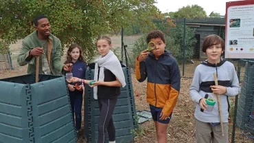un groupe d'enfants et leur animateur sont devant des composteurs
