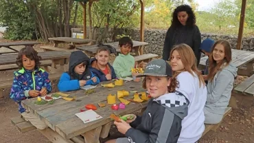 un groupe d'enfants et leur animatrice sont assis autour d'une table avec des éléments naturels