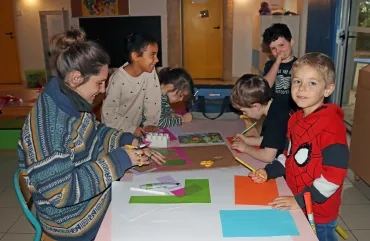 un groupe d'enfants et leur animatrice découpent du papier coloré