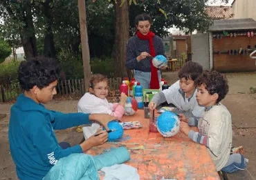 un groupe d'enfants et leur animatrice peignent des ballons de baudruche recouverts de papier maché