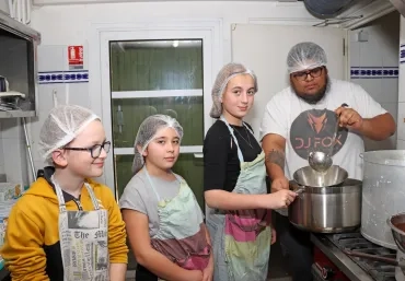 un groupe d'enfants et leur animateur séparent le caillé du petit lait en cuisine