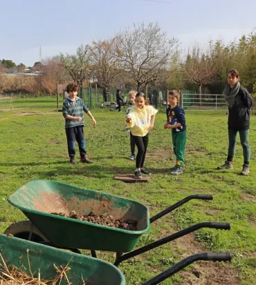 un groupe d'enfants et leur animatrice visent des brouettes avec du crottin
