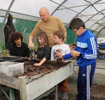un groupe d'enfants et leur animateur remplissent de terre un objet en métal