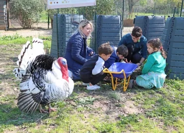 Un groupe d'enfants et leurs animateurs sont près des composteurs avec un dindon en rpemier plan