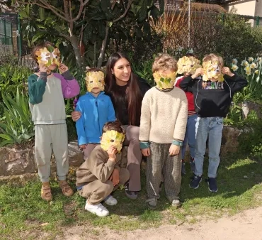 Un groupe d'enfants et leur animatrice posent avec eds masques décorés par des feuilles sur leur visage