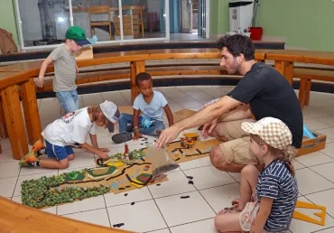 un groupe d'enfants et leur animateur sont au sol avec des éléments de maquette
