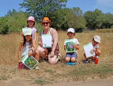 un groupe d'enfants et leur animatrice sont dans l'herbe et montrent des photos de plantes