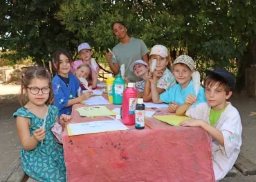 un groupe d'enfants et leur animatrice sont autour d'une table et montrent des plumes