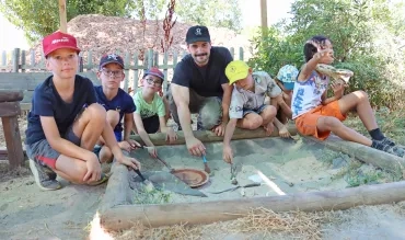 Un groupe d'enfants et leur animateur posent derrière un bac à sable avec des pinceaux