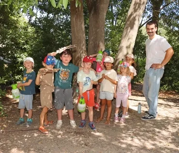 Un groupe d'enfants et leur animateur montrent des pulvérisateurs à côté d'un arbre