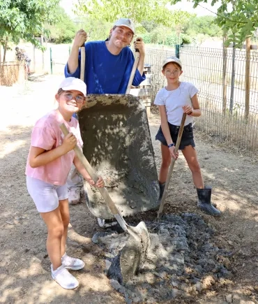 un groupe d'enfants et leur animateur vident une brouette de boue