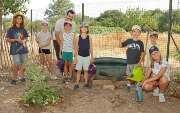 Un groupe d'enfants et leur animateur posent devant une bassine avec des arrosoirs