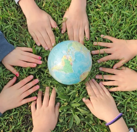 Mains d'enfants autour d'un globle terrestre posé sur une surface enherbée