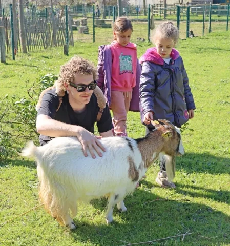 deux enfants et leur animateur caressent une chèvre