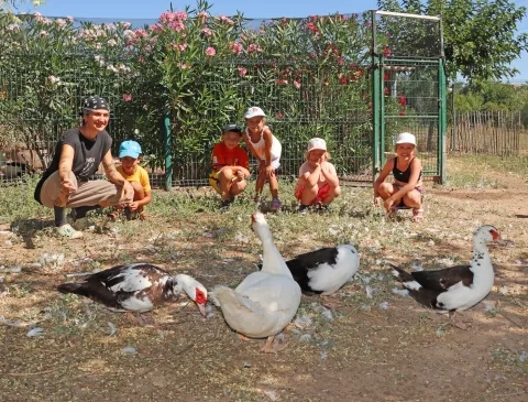 Un groupe d'enfants et leur animatrice sont derrère des canards de Barbarie